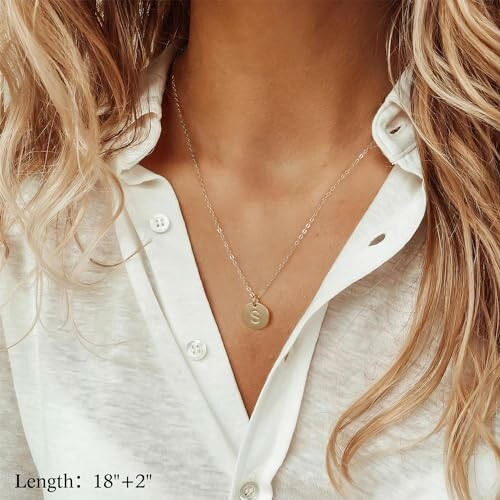 Woman wearing a gold initial pendant necklace over a white shirt.