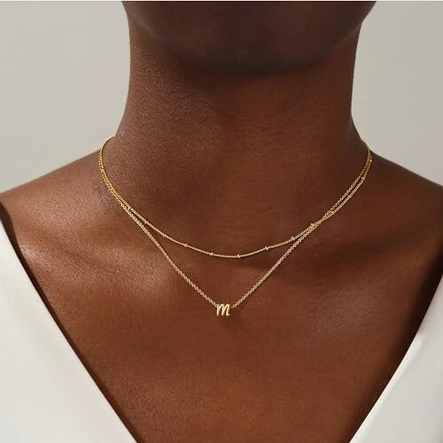 Person wearing a gold layered necklace with an 'm' pendant