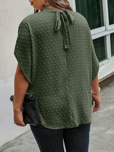 Woman wearing a green textured blouse with a bow at the back, holding a black clutch.