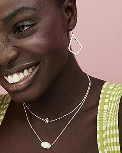 Woman wearing earrings and layered necklaces, smiling.