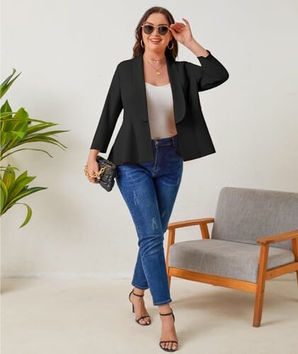 Woman in black blazer and jeans standing near a chair.